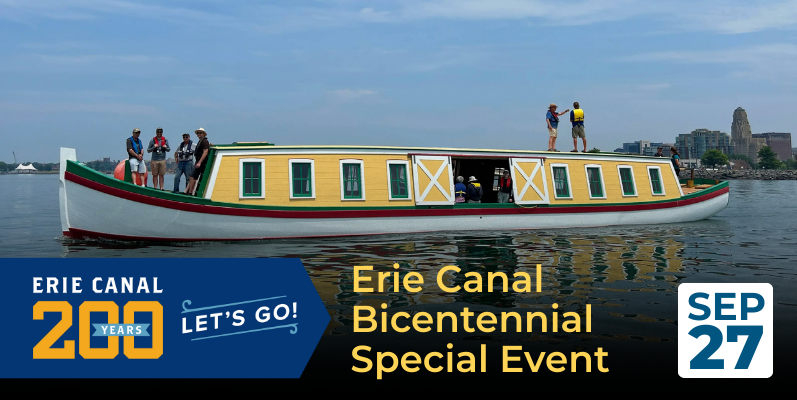 9 People on a colorful boat celebrating Erie Canal Bicentennial with city skyline in the background.