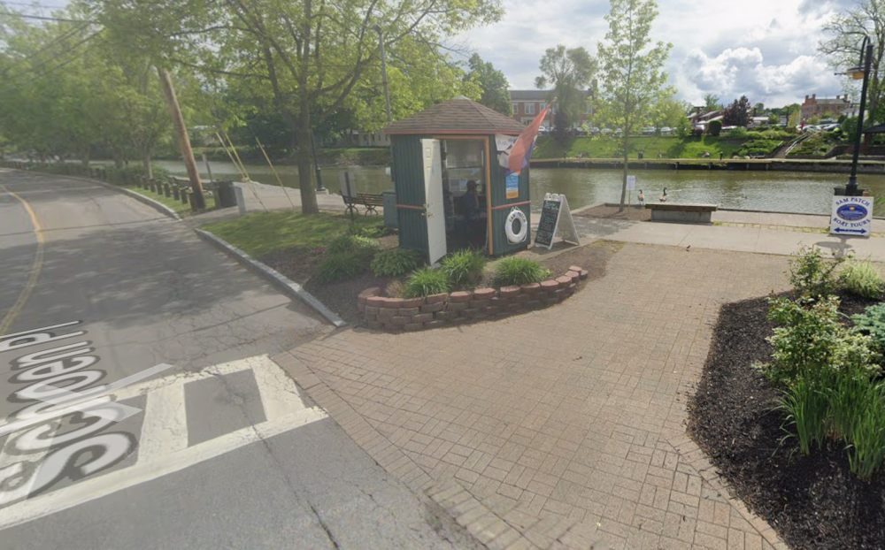 Small canal booth surrounded by greenery, near a road and the water.