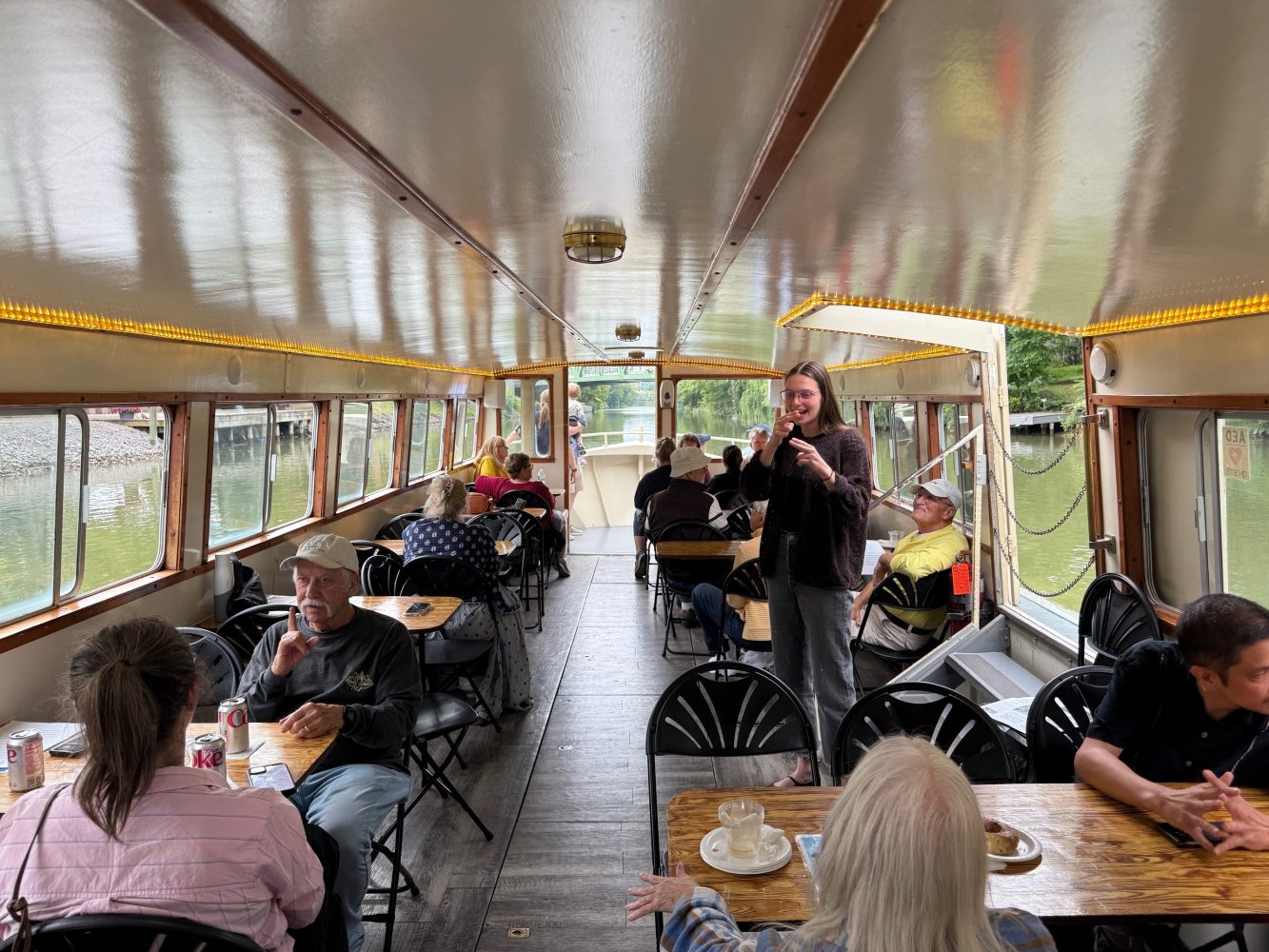 Inside a boat with people seated at tables, enjoying a scenic cruise.